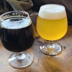 Two glasses of beer on a wooden table: one dark stout and one golden ale.