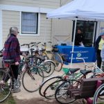 Bicycles parked near a tent at an outdoor community event with people gathered.
