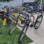 Assortment of bicycles parked on grass and concrete near a building.