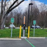 Electric vehicle charging station in a parking lot with trees and blue sky.