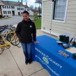 Woman stands next to a blue table displaying park county materials near historic buildings.