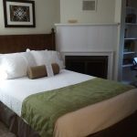 Bedroom with large white bed, brown headboard, and fireplace mantel.