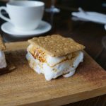 Scones with whipped cream and cinnamon on a wooden cutting board, near coffee.