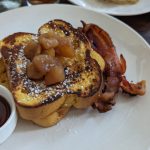 French toast topped with caramelized apples and bacon on a white plate.