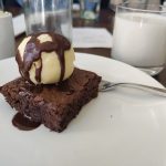 Chocolate brownie topped with a scoop of vanilla ice cream and chocolate sauce, served on a white plate.