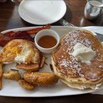 Fluffy pancakes topped with whipped cream served with fried eggs and roasted potatoes.
