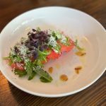 Garnished tomato and arugula salad served on a white plate.