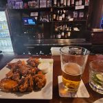 Plate of crispy fried chicken on a table in front of a bar with drinks and liquor shelves.