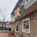 Flags fly from a building with stone facade and brick walkway on an overcast day.