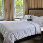 Luxurious hotel room with large bed, beige curtains, and bright windows.