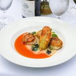 Seared scallops and roasted zucchini served in a vibrant tomato sauce on a white plate.