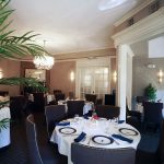 Elegant dining room with white tablecloths, chandeliers, and lush green plants.