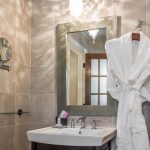 Bathroom vanity with mirror, sink, and white bathrobe hanging nearby.