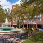 Hotel facade with fountain and green lawn under leafy trees.
