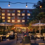 Modern brick apartment building exterior at dusk with outdoor patio seating and string lights.