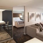 Modern hotel suite interior showing living area, bedroom view, and entryway.