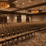 Large, carpeted conference room with rows of empty seating and ornate chandeliers.