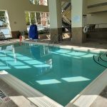 Indoor swimming pool with bright sunlight streaming through large windows.