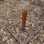 Wooden post in a square frame on a forest floor covered with dry leaves.