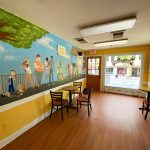 Vibrant mural of a tree and people in a bright, empty room with wooden floors.