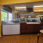 Cafe interior with a display case, counter, and seating area.
