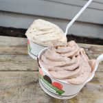 Two cups of creamy, swirled ice cream on a rustic wooden table outdoors.