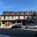 Historic two-story building with dormers and storefronts on a sunny city street.