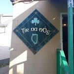 Irish-themed sign with shamrock and harp reading "Tír na nÓg" on a building exterior.
