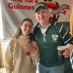 Woman and man smiling in front of a Guinness banner at an event.