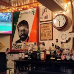 Bar interior with sports TV, liquor shelves, and vintage decor.