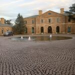 Brick building with fountain in paved courtyard under a cloudy sky.