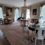 Elegant, ornate dining room with chandelier, large windows, and patterned rug.