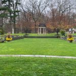 Manicured lawn leading to a classical gazebo in a park setting with trees.