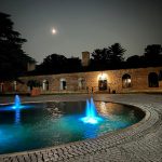 Nighttime fountain display in a courtyard with historic stone walls and moonlight.