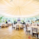 Elegant wedding reception setup under a draped, illuminated ceiling with floral centerpieces.