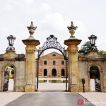 Ornate stone archway entrance to a historic, brick-built courtyard under a cloudy sky.