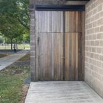 Modern wooden garage door next to a brick building with trees in the background.