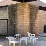 Outdoor patio area with textured brick walls, white tables and chairs under a wooden overhang.