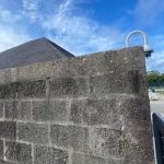 Textured gray concrete block wall under a bright blue, cloudy sky.