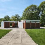 Pavilion structure with brick and white siding, set on a grassy area under blue sky.