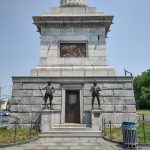 Monument with soldiers flanking the entrance beneath a tall stone obelisk.