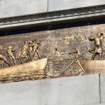 Bronze relief sculpture depicting figures rowing a boat on rough, wavy water.