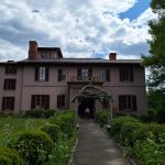 Stone manor house with garden path and archway under a cloudy sky.