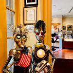 Two vintage robot figures displayed in a shop with framed art on the wall.