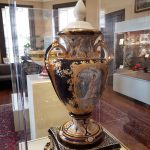 Ornate, antique porcelain vase displayed in a glass museum case.