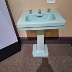 Vintage mint green pedestal sink in a museum or historical setting.