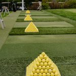 Golf practice range with pyramids of yellow golf balls on green turf.