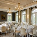 Elegant ballroom set for a formal event with white tables and ornate chandeliers.