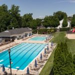 Outdoor resort pool area with multiple pools, lounge chairs, and green lawn under a blue sky.