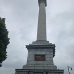 Tall stone monument with a statue on top against an overcast sky.